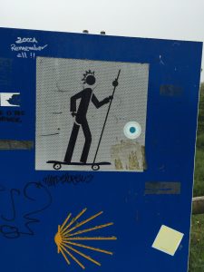 This Camino directional sign has been altered with skateboard and hairdo. 